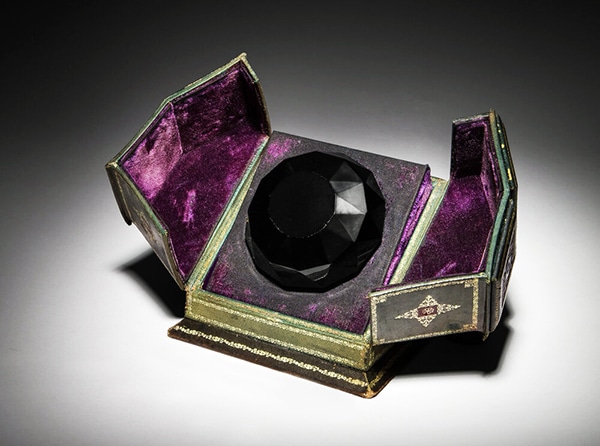 A 1926 Baccarat for Isabey “Tresor Cache” presentation of Lys black crystal perfume bottle and stopper as a faceted jewel with cord seal, label and tooled leather box sold for $56,250 at an auction held July 11 by Perfume Bottles Auction in New York City