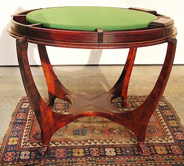 An impressive George Hunzinger Mahogany flip top yacht game table, c.1890s. This superb round gaming table has a mahogany veneered top which reverses to reveal a gaming table with a green baize surface, surrounded by wells for gaming pieces. The tabletop swivels on rods through two of the four leg top terminals. The other two leg-top terminals have a metal spring-loaded catch mechanism that holds the tabletop in place and allows it to swivel when the catch is depressed.