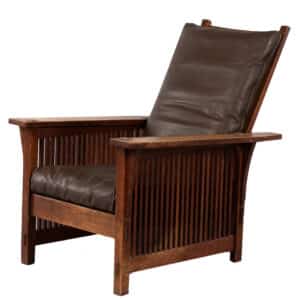 Gustav Stickley "Model #367" Spindle Morris Chair, Eastwood, New York, 1904-1912, quartersawn oak, with corbel supports under each arm, thru-tenon construction, replaced sling seat with recovered leather seat and back cushion, original finish, marked with red decal sold for $2,635 at a 2020 Skinner auction.