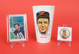 A gallery of giveaways: a 1973 Brooks Robinson Slurpee cup is flanked by a 1970 Kellogg’s card of Gale Sayers and a 1962 Henry Aaron Salada Tea coin.