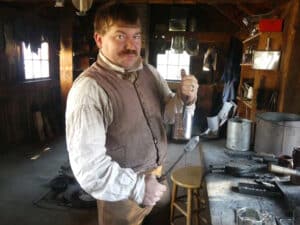 Here, the body of the cup was shaped and has been soldered to keep its shape and to make it watertight. The tool in his right hand is the soldering copper which has been heated in the charcoal fire to melt the solder.