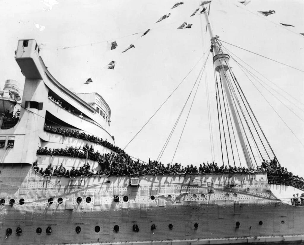 During World War II, the Queen Mary was stripped down, painted camouflage grey, and used to transport troops and prisoners of war. Her speed made her a success, 
outstripping the U-boats sent to block her and earning 
the moniker the “Grey Ghost.” In this image, 
Allied soldiers wave aboard the converted vessel.