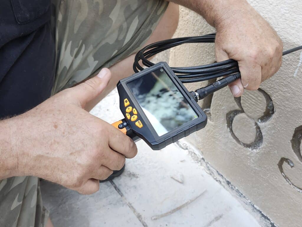 Jack Stanley is holding a borescope, to check the drill hole for evidence of the copper box. Several exploratory holes had been drilled, and one had hit something that seemed to be it. However this was difficult to confirm with the borescope, so owner Lou Pektor grabbed the demolition hammer, and started chipping away at the façade to open a larger hole.