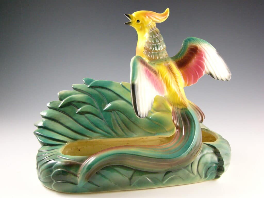 Yellow tropical bird, atop a TV lamp doing double-duty as a planter.