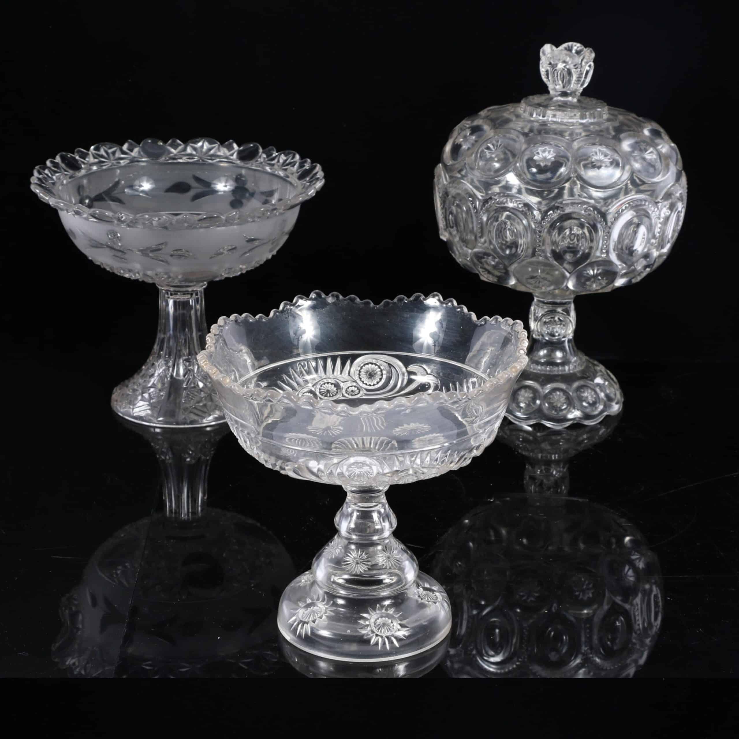 Early American pressed glass EAPG large clear bullseye pattern covered compote candy dish along with two other compoted pedestal bowls; 3pc group. 12"H x 8"W (covered) photo: ripleyauctions.com
